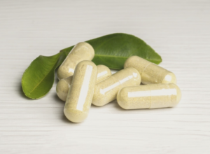 Capsule di berberina naturale contenenti estratti vegetali, adagiate su una superficie bianca con foglie verdi sullo sfondo, simbolo di benessere e nutraceutica.