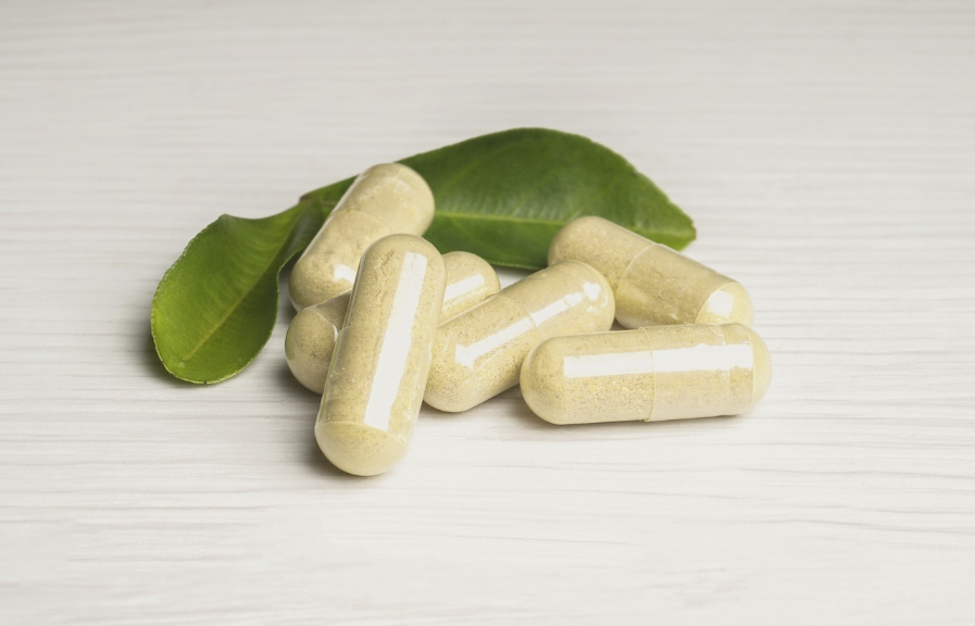 Capsule di berberina naturale contenenti estratti vegetali, adagiate su una superficie bianca con foglie verdi sullo sfondo, simbolo di benessere e nutraceutica.